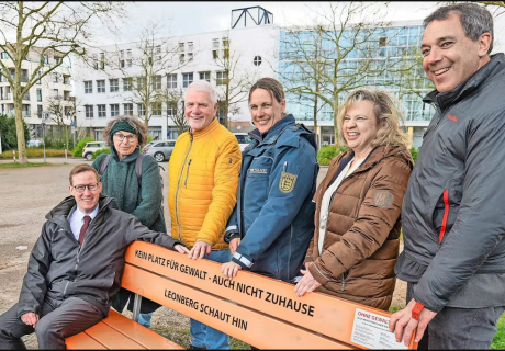 Sechs Personen stehen draußen hinter einer Orangenen Bank mit der Aufschrift "Kein Platz für Gewalt - Auch nicht Zuhause; Leonberg schaut hin"